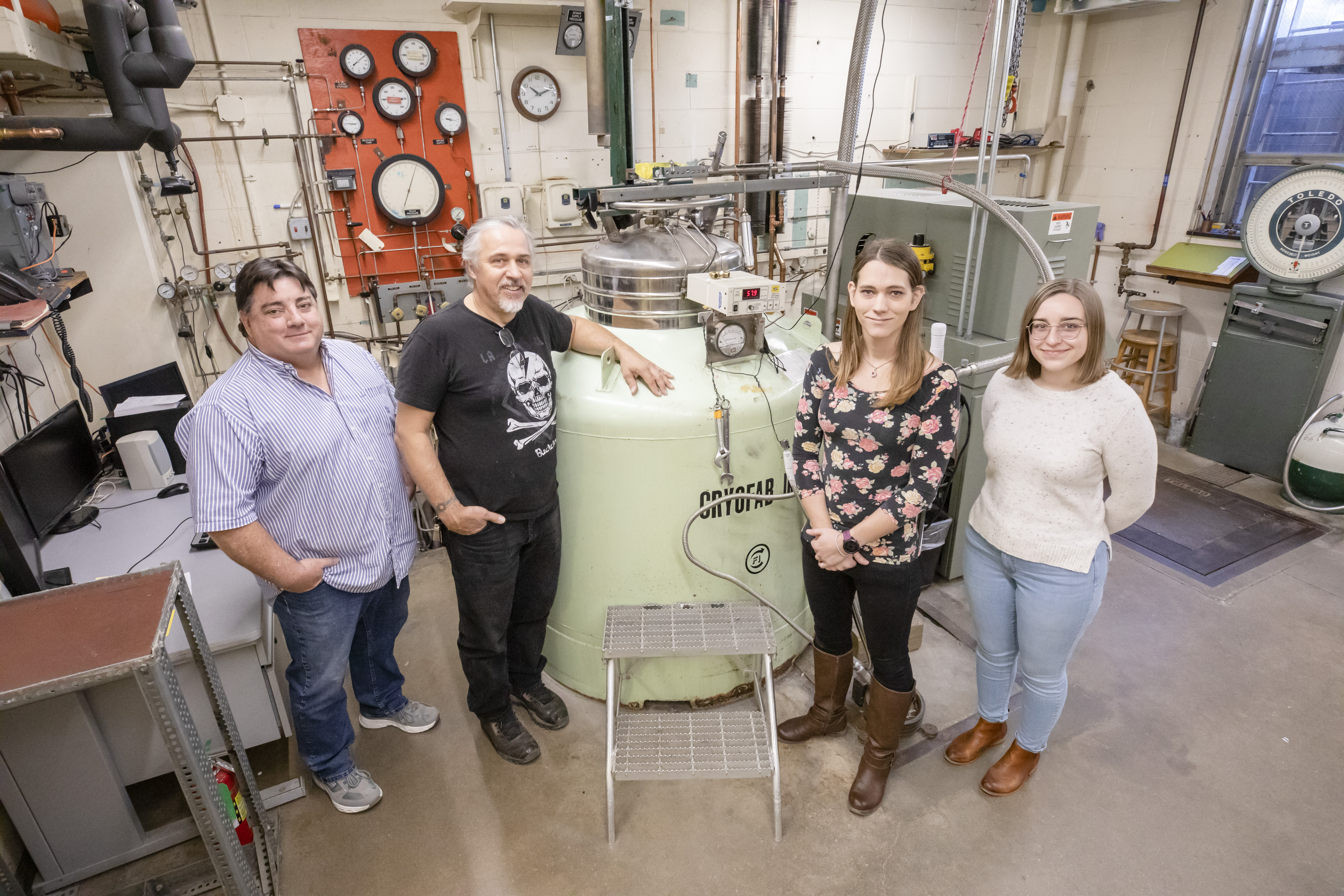 The Illinois Physics Liquid Helium Facility team poses for a photo in the main facility on the first floor of Loomis Lab. Pictured left to right are cryogenics technician Kelly Sturdyvin, research engineer Eric Thorsland, cryogenics programmer Nikki Colton, and Illinois Physics undergraduate Anna Przybyl.